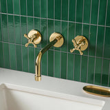 Gold faucet and handles on a green tiled wall with a white sink.