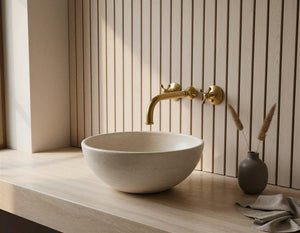Bathroom sink with gold faucet against a wooden wall