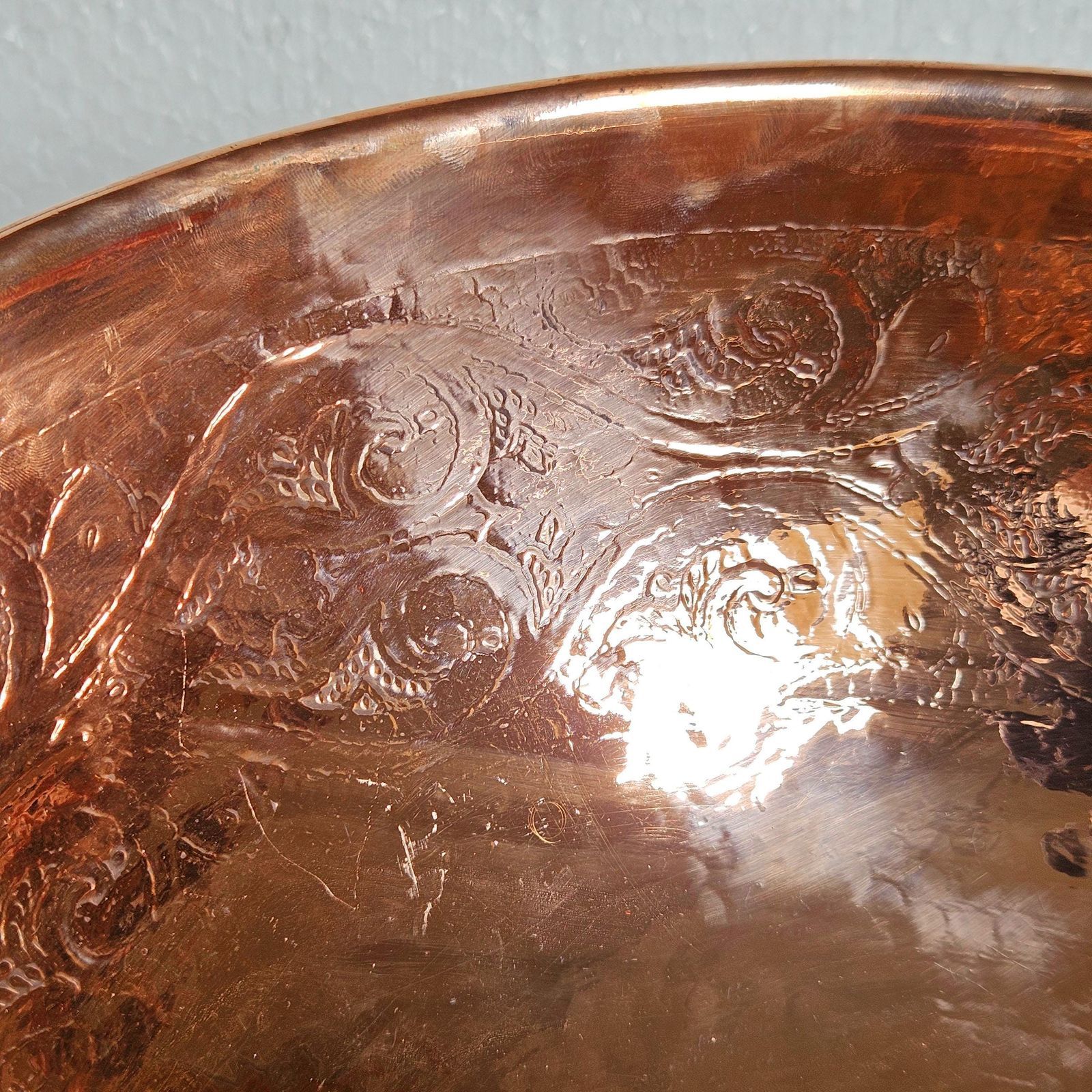 Close-up of a copper bowl with embossed designs on a light gray background
