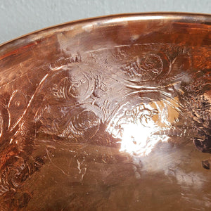 Close-up of a copper bowl with embossed designs on a light gray background