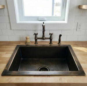 Stainless steel kitchen sink with bronze faucet in a modern kitchen setting.