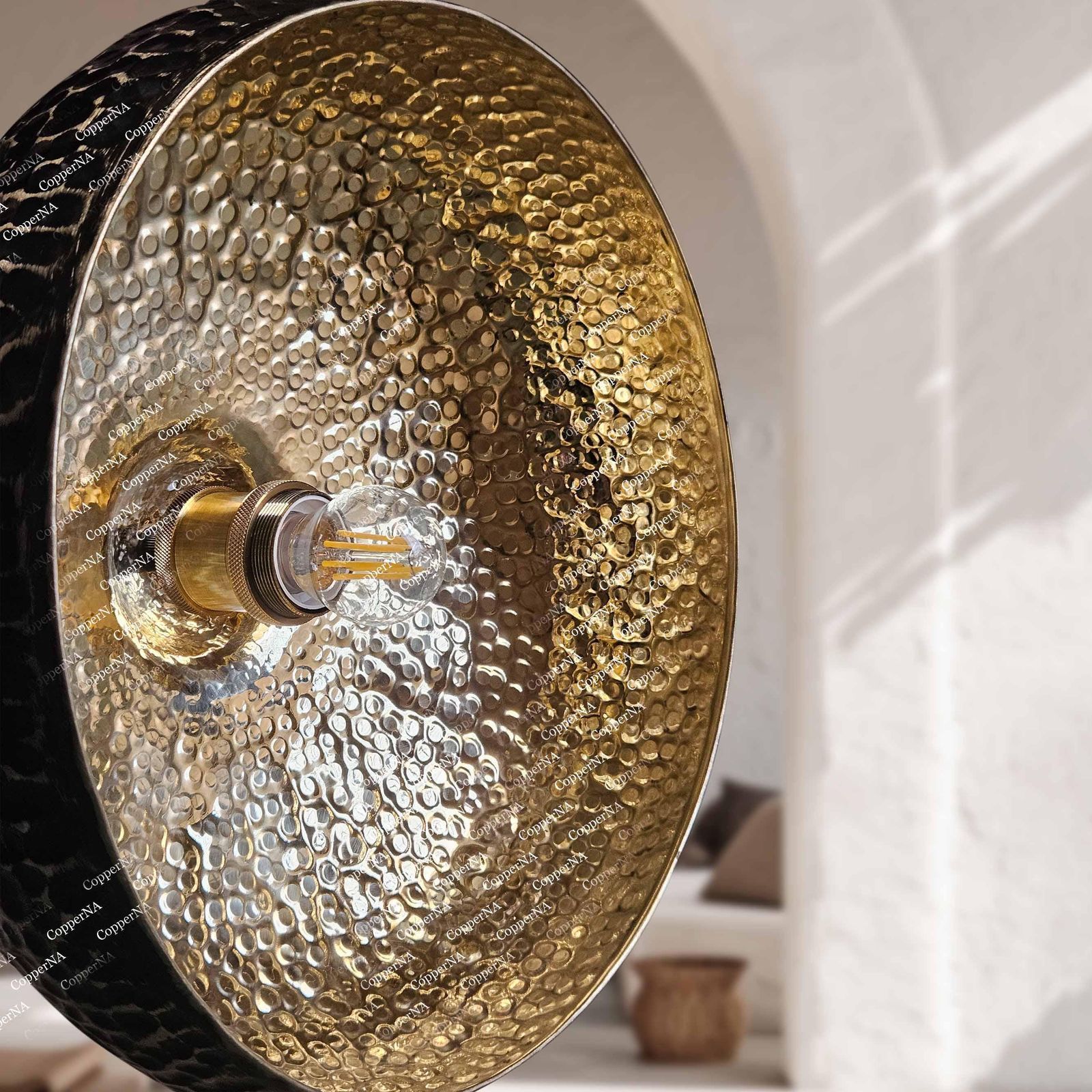 extured antique bronze dome pendant lamp suspended from a black cord against a soft white stucco background.