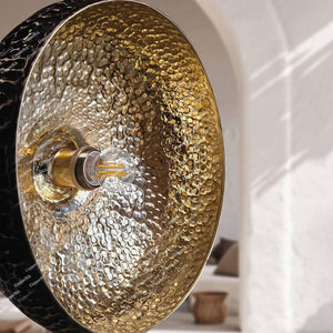 extured antique bronze dome pendant lamp suspended from a black cord against a soft white stucco background.