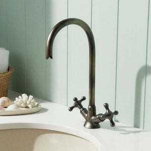 Bronze faucet on a white sink with a light green wall in the background