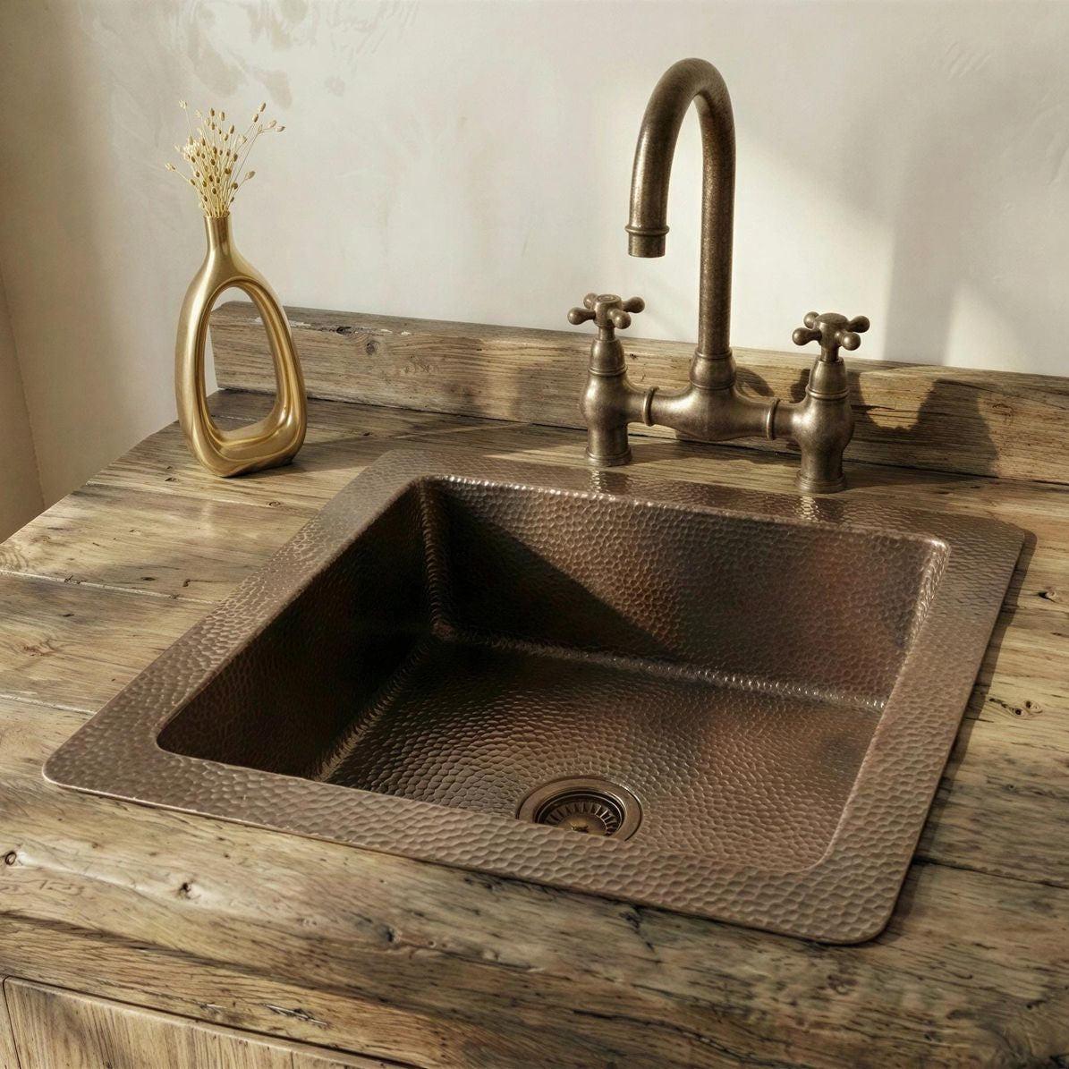 Patina brass sink on a wooden countertop with a gold vase and faucet.