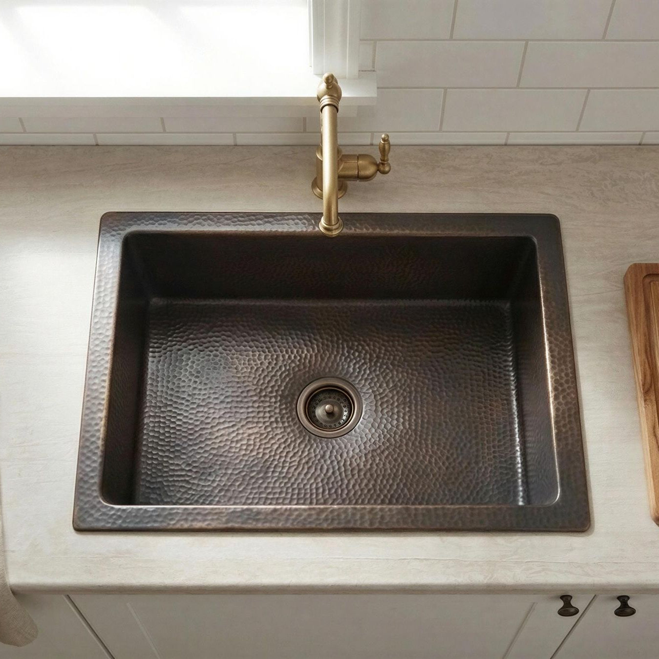 Copper kitchen sink with gold faucet on a light-colored countertop.