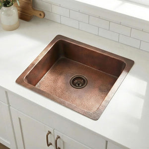 Copper kitchen sink on a white countertop with a tiled backsplash.