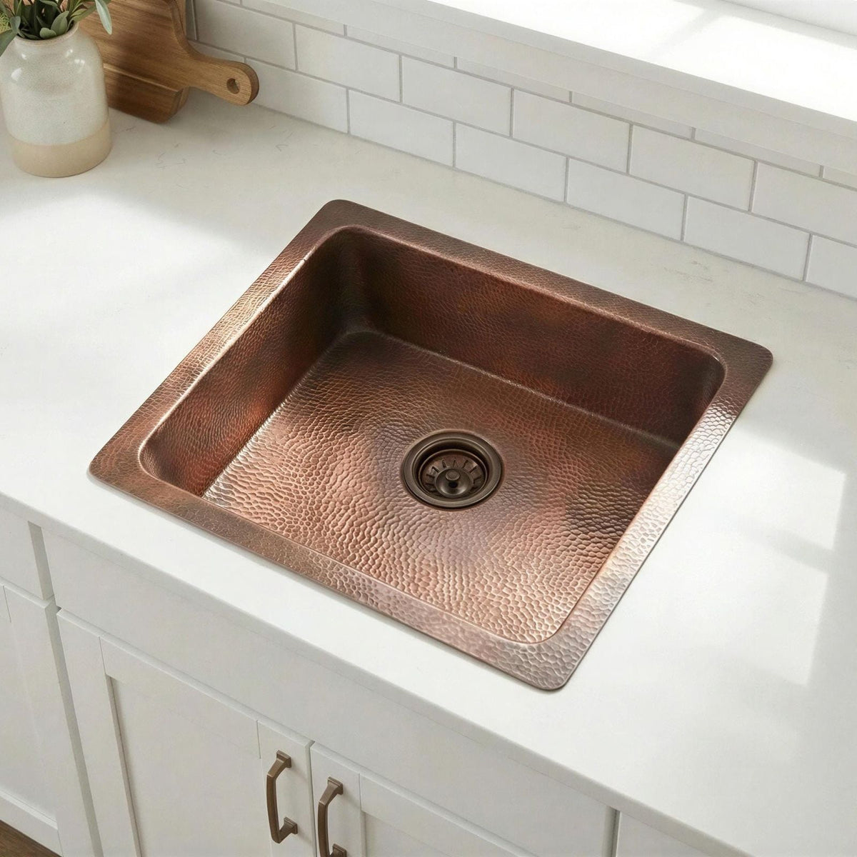 Copper kitchen sink on a white countertop with a tiled backsplash.