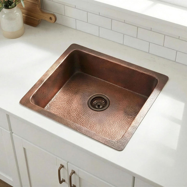 Copper kitchen sink on a white countertop with a tiled backsplash.
