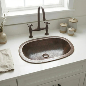 Copper sink on a white countertop with a window in the background