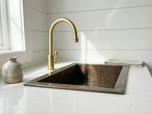 Antique brass kitchen sink with gold faucet on a white countertop