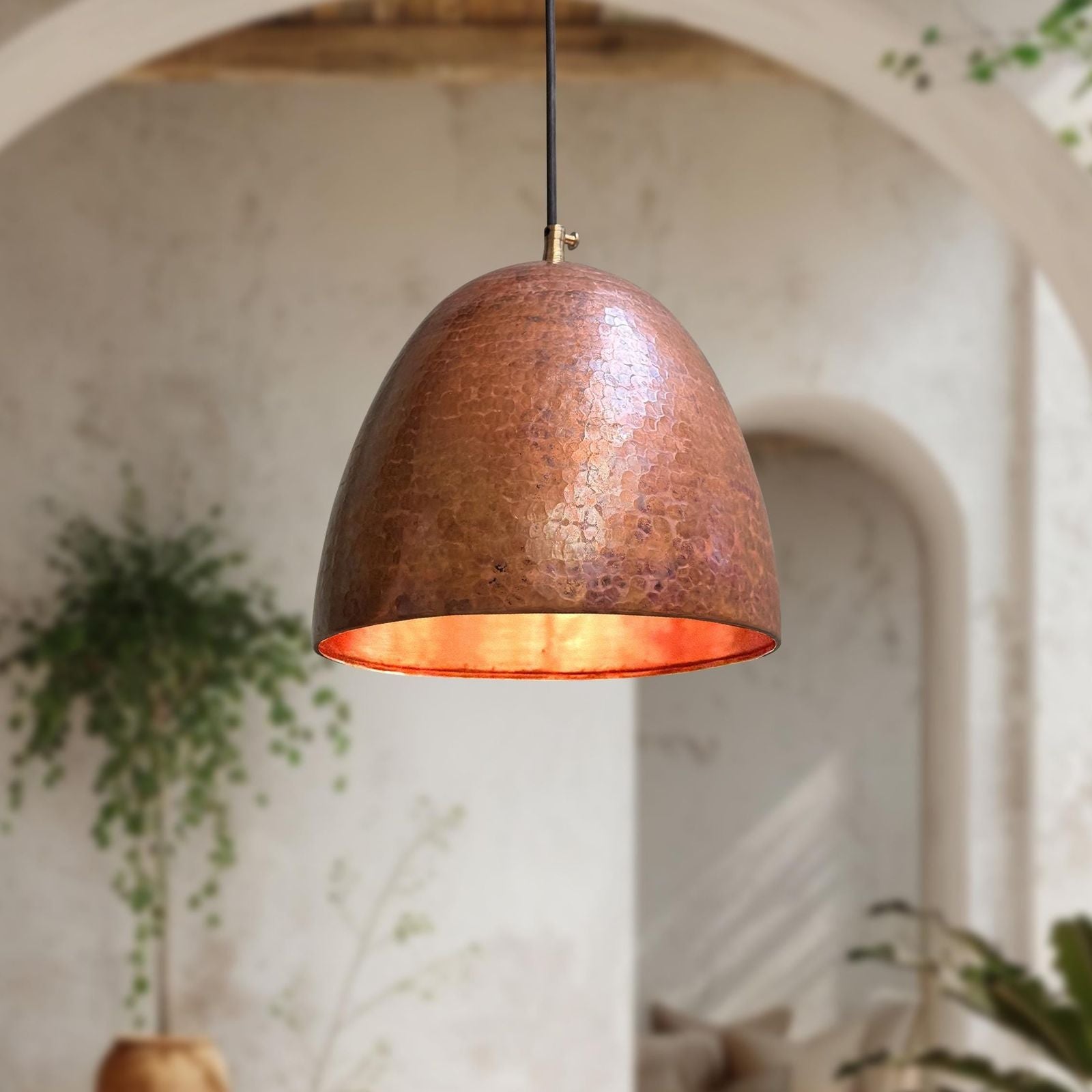 Copper pendant light hanging in a room with plants and arches.