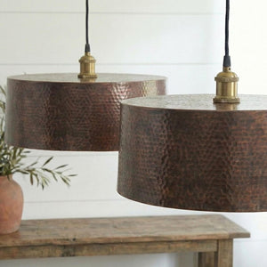 Two copper pendant lights hanging above a wooden table with a white wall background.