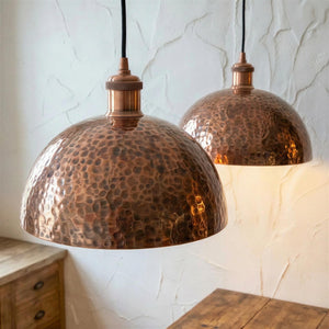 Two copper pendant lights hanging against a textured white wall.