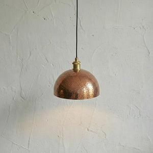 Copper pendant light hanging against a textured white wall