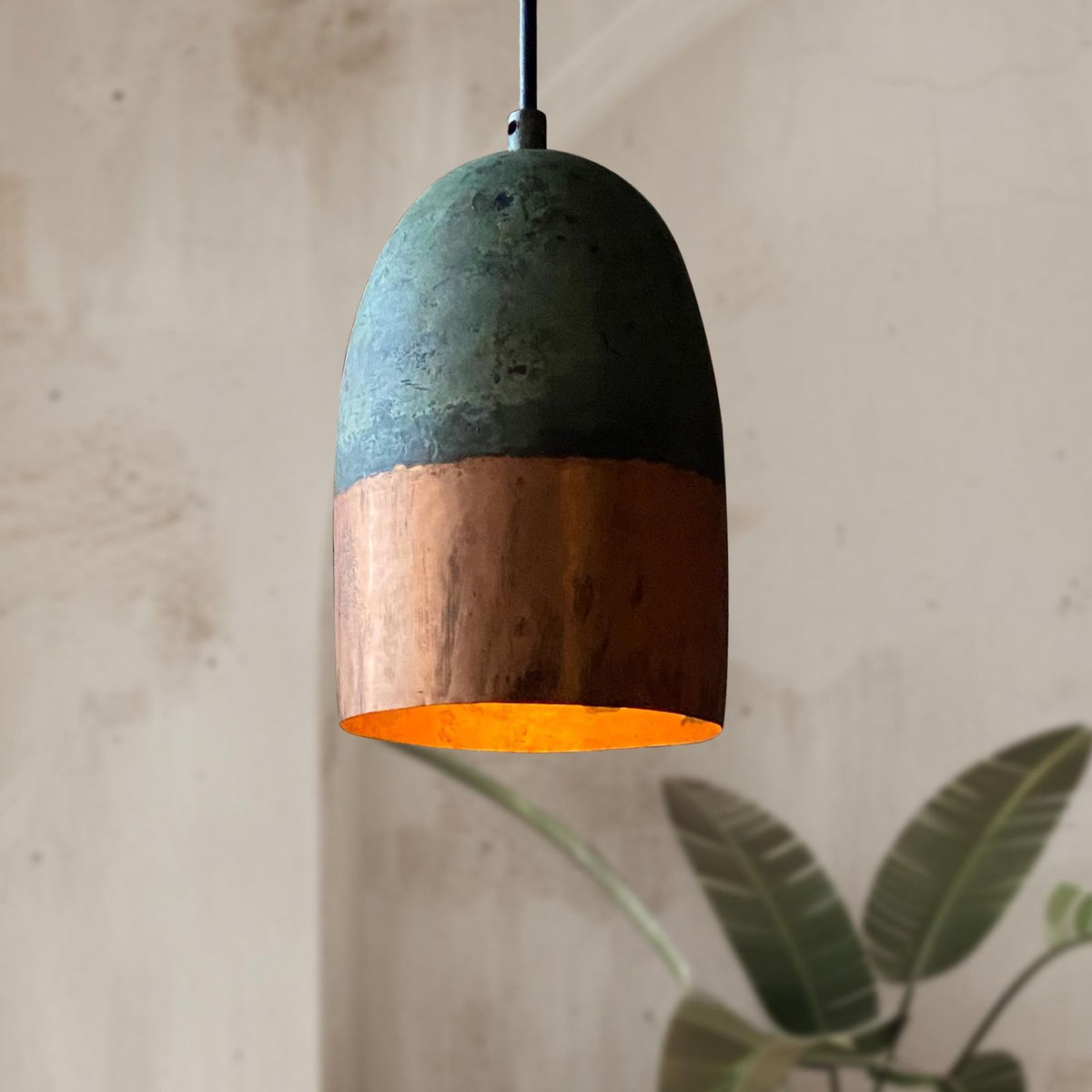 Pendant light with green top and copper bottom on a neutral background
