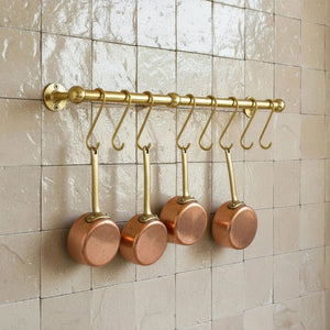 Set of copper pots hanging on a gold rack against a tiled wall.