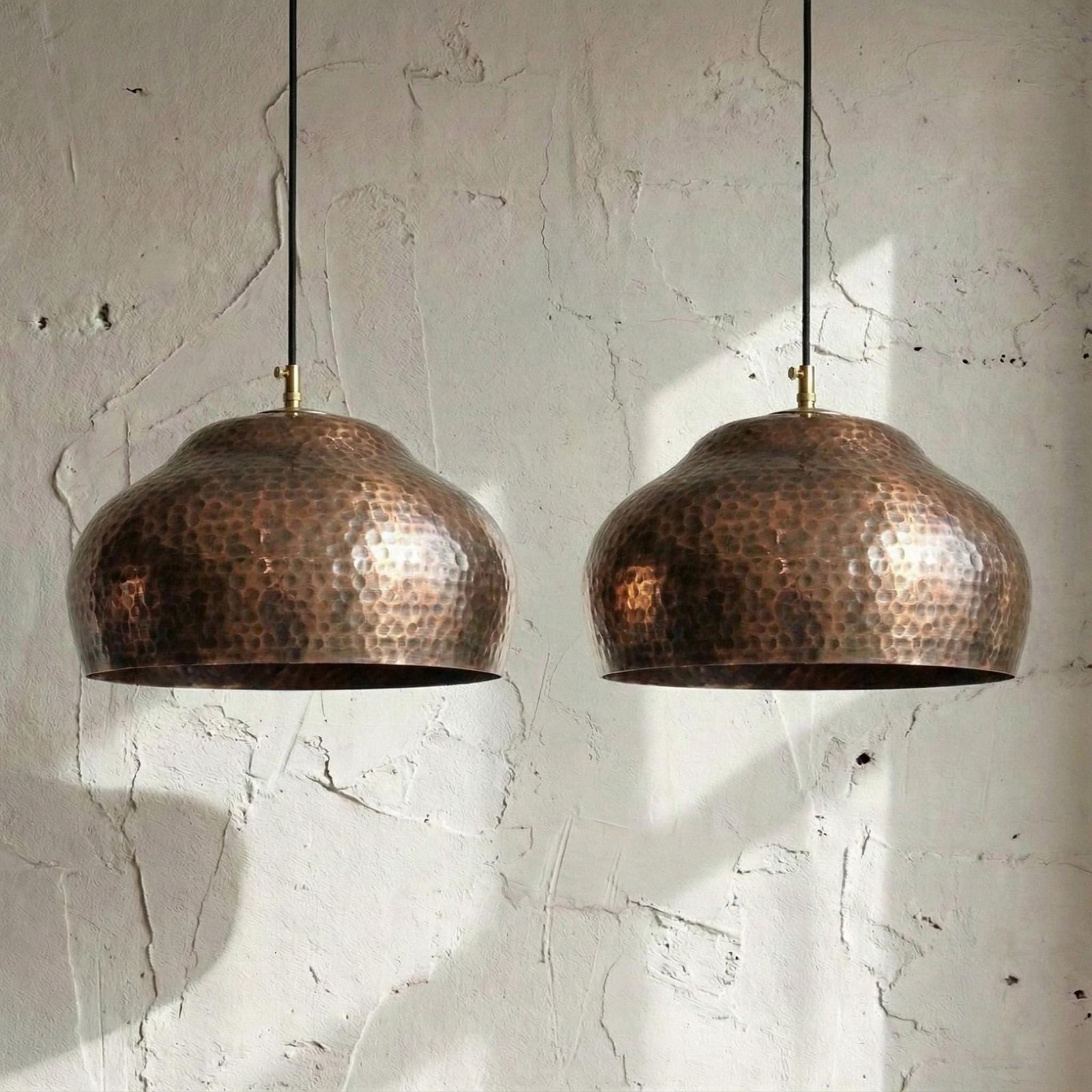 Two copper pendant lights hanging against a textured white wall.