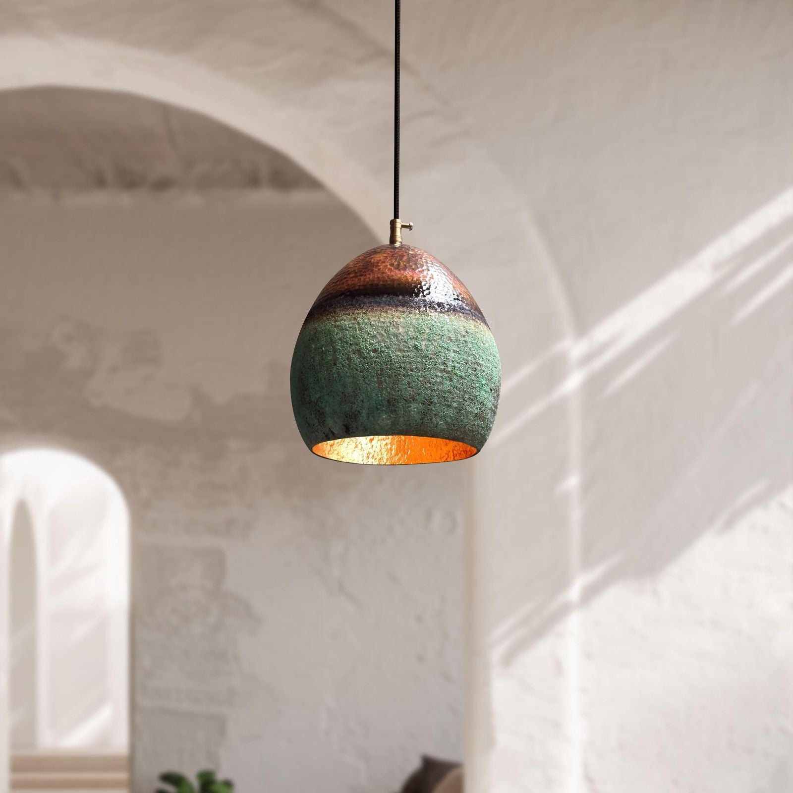 Green pendant light with gold interior hanging against a white wall.