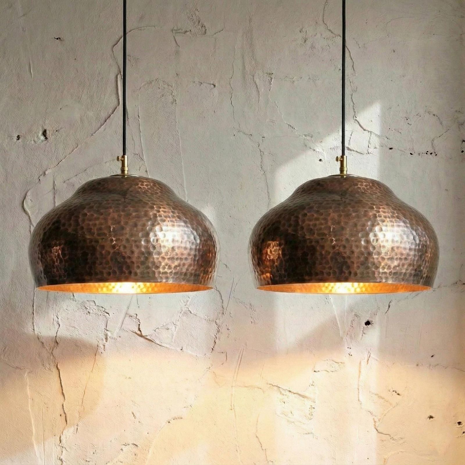 Two copper pendant lights hanging against a textured wall.