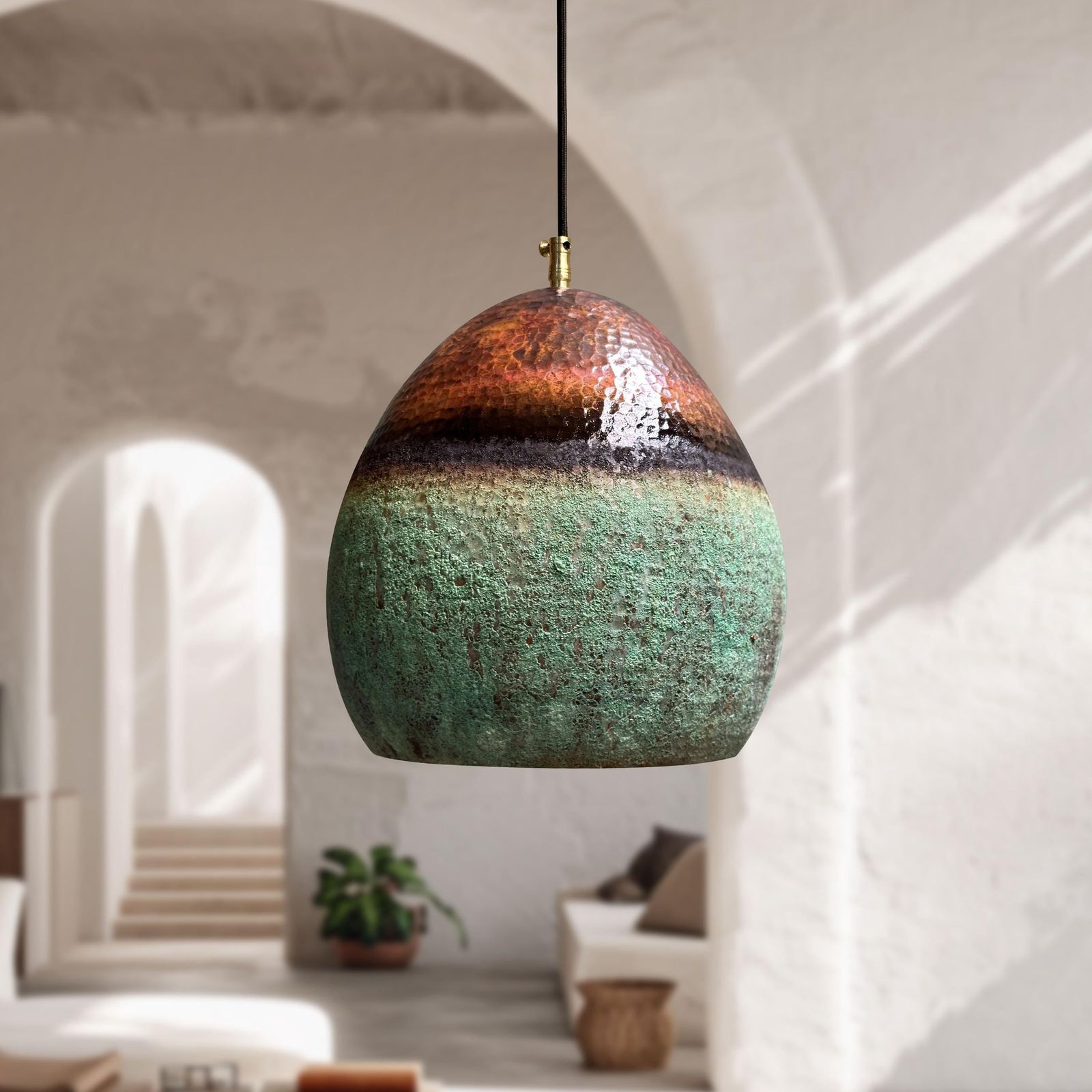 Decorative pendant light with a textured design hanging in a room with white walls and a plant.