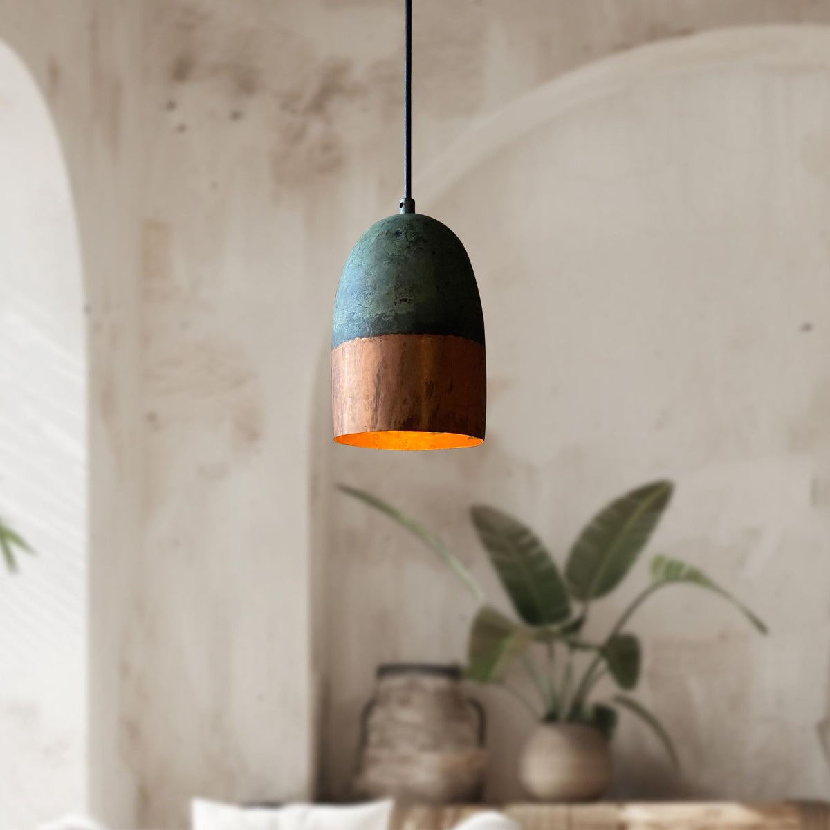 Pendant light with green and wooden design hanging in a room with plants and a textured wall.