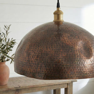 Copper pendant light with a textured surface on a wooden table.