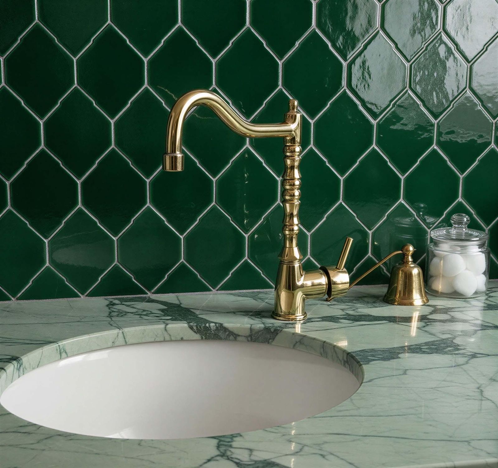Gold faucet on a marble sink with green tiled wall