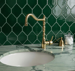 Gold faucet on a marble sink with green tiled wall