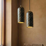 Two pendant lights with textured black and gold shades hanging against a brown wall.
