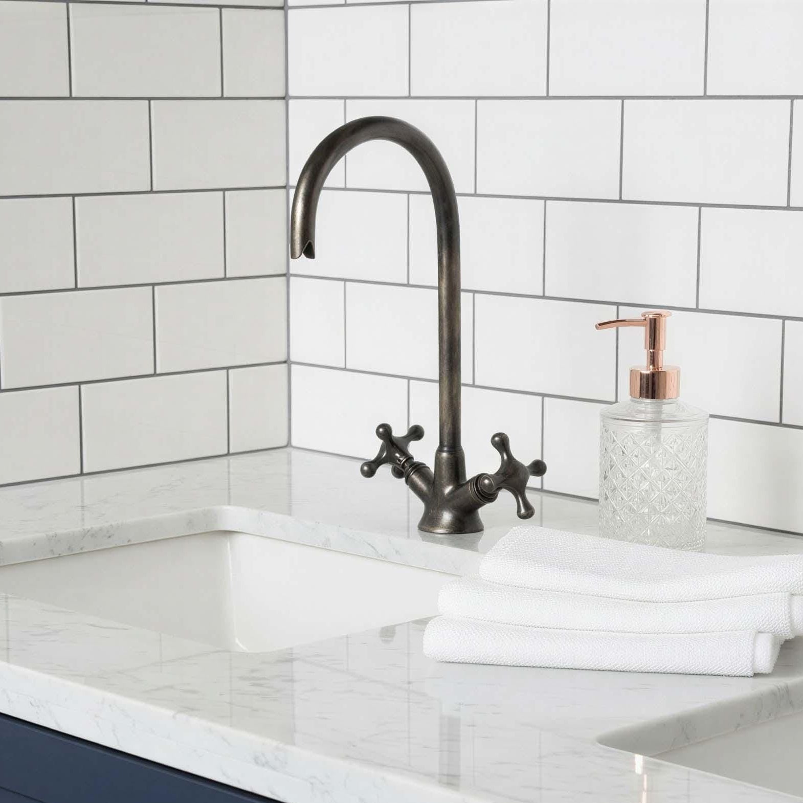 Bathroom sink with white marble countertop, dark blue cabinets, and white tiled wall.