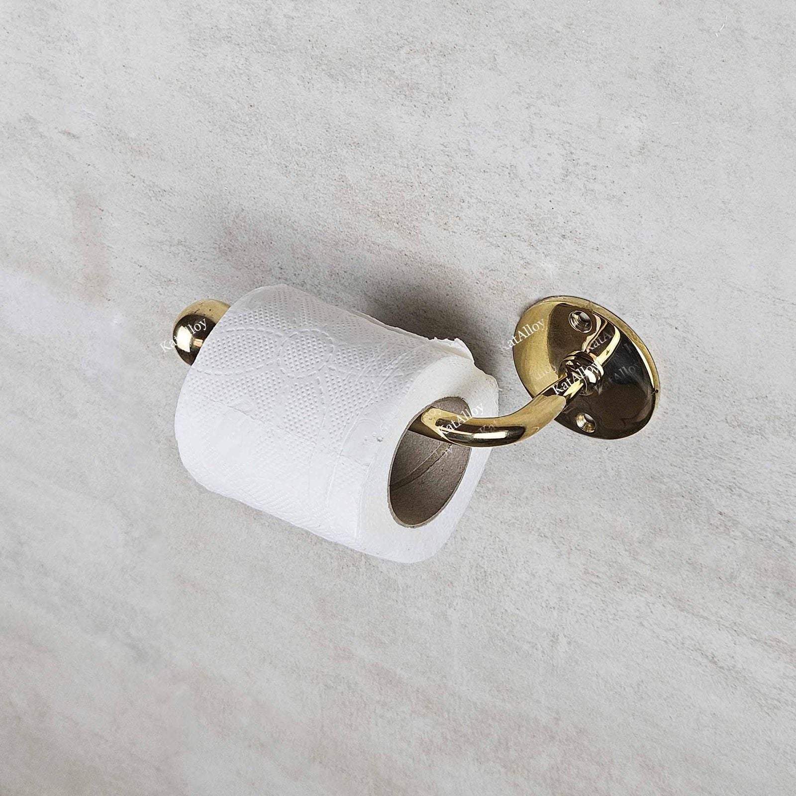 Gold toilet paper holder with a roll of white toilet paper on a light gray wall.