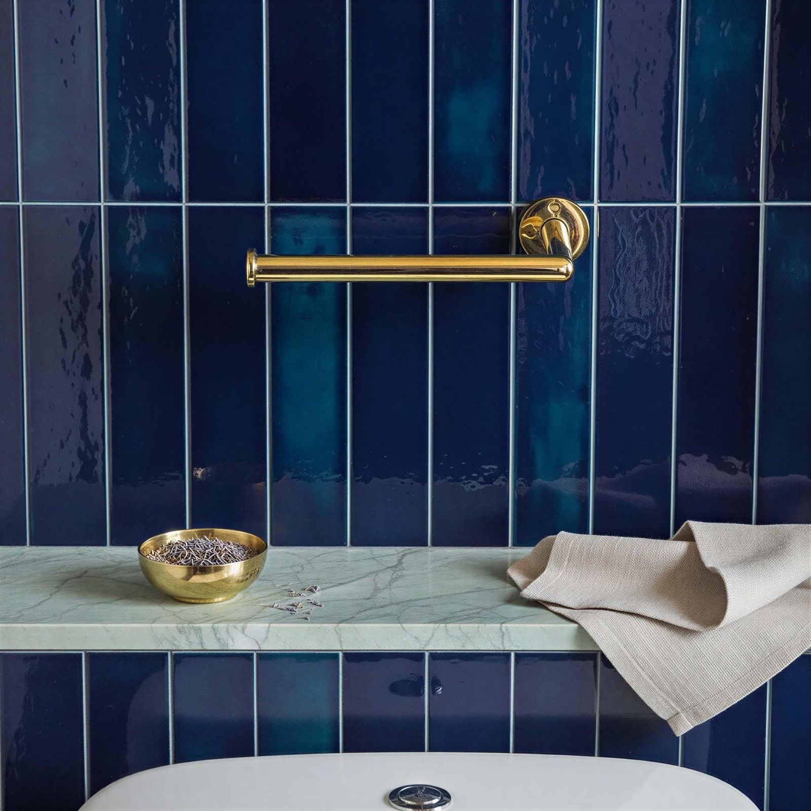 Bathroom with blue tiles, gold handle, and marble shelf.