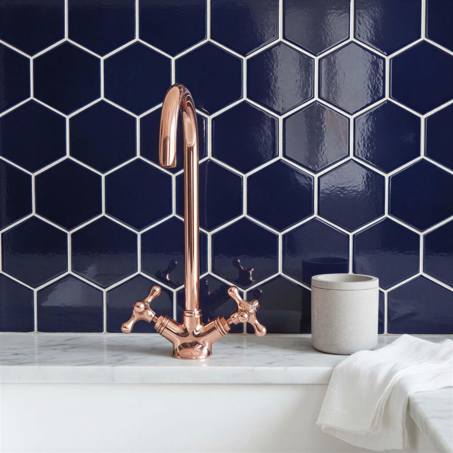 Bathroom setting with a copper faucet against a blue hexagonal tile wall.