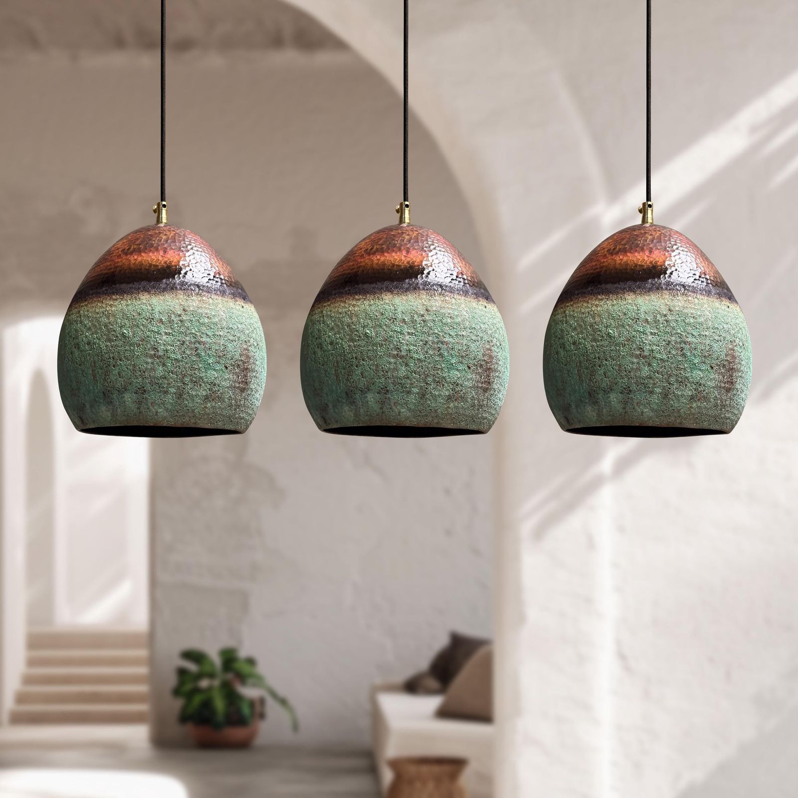 Three ceramic pendant lights hanging in a room with a white wall and plant in the background.