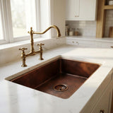 Copper kitchen sink with brass faucet in a bright kitchen setting