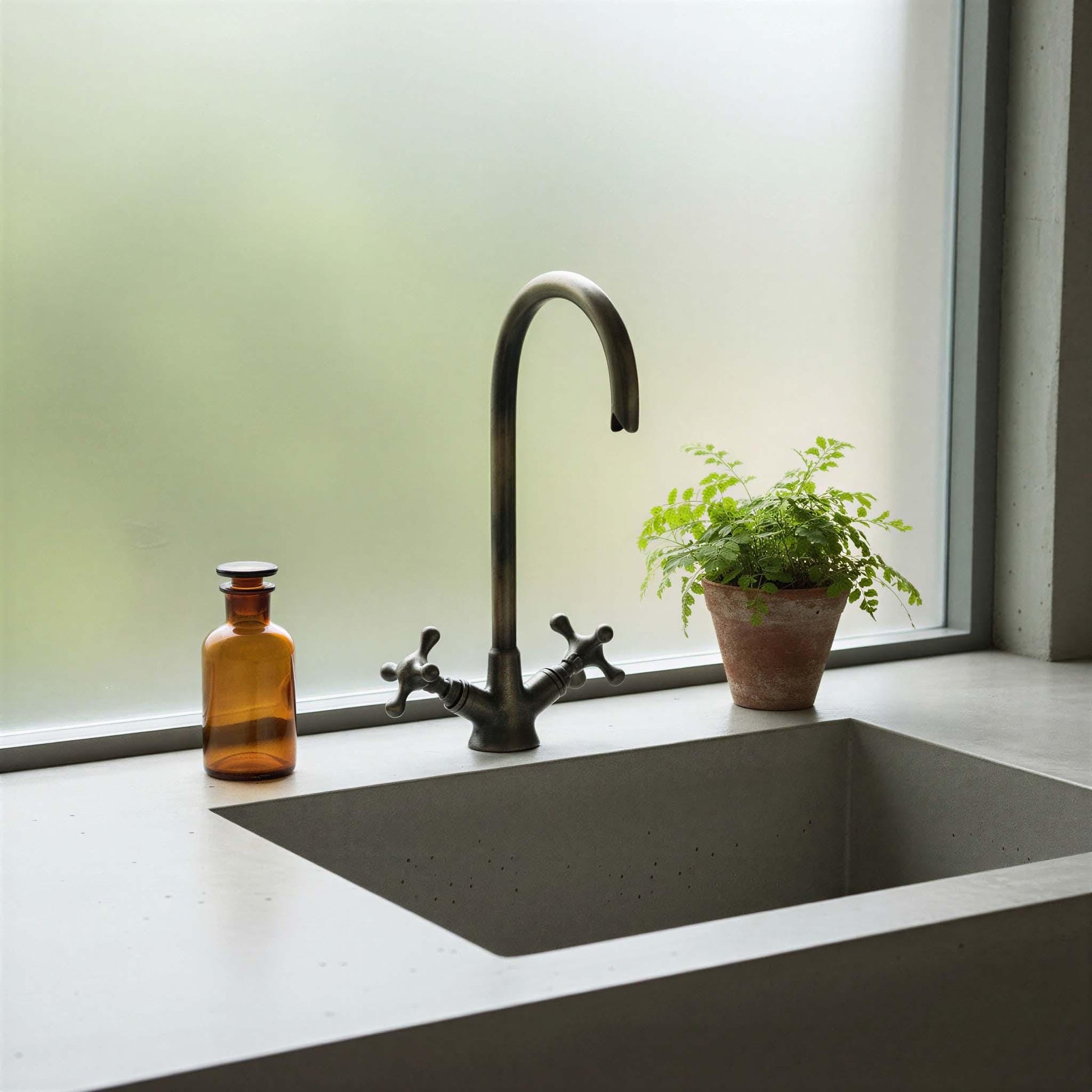Modern kitchen sink with black faucet and a plant on a light-colored countertop.