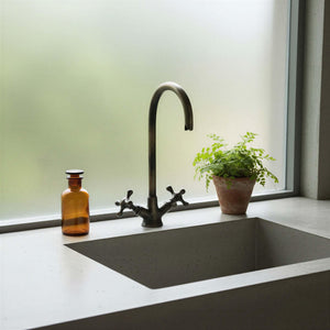 Modern kitchen sink with black faucet and a plant on a light-colored countertop.