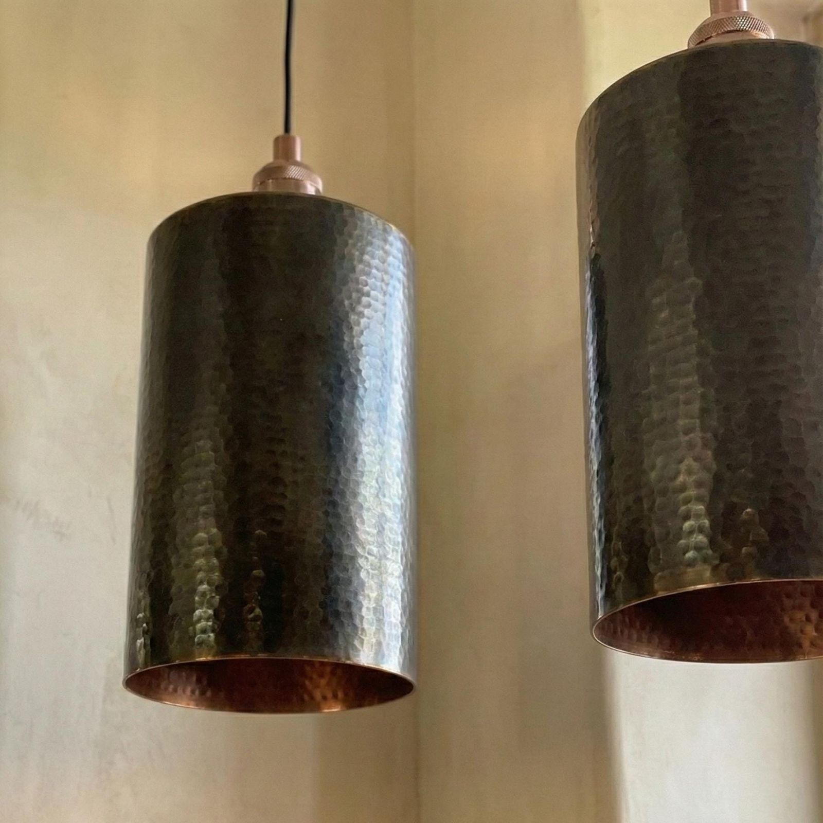 Two dark bronze pendant lights hanging against a beige wall.
