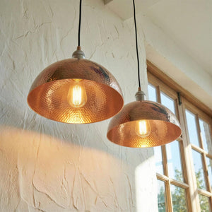Two copper pendant lights hanging in a room with a window in the background.