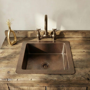 Patina Brass sink on a wooden countertop with a gold vase and faucet.