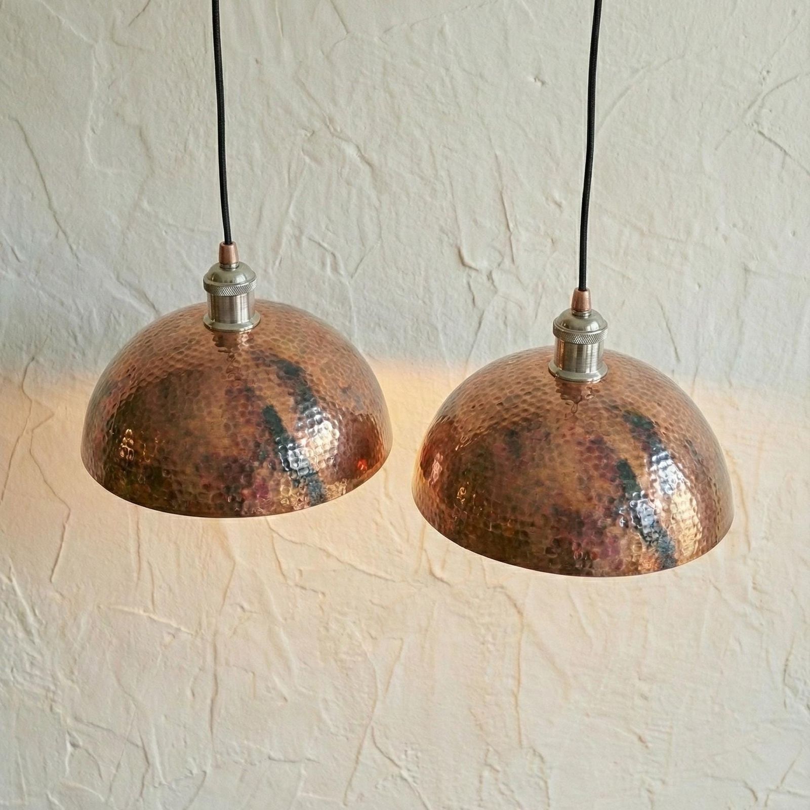 Two copper pendant lights hanging against a textured white wall.