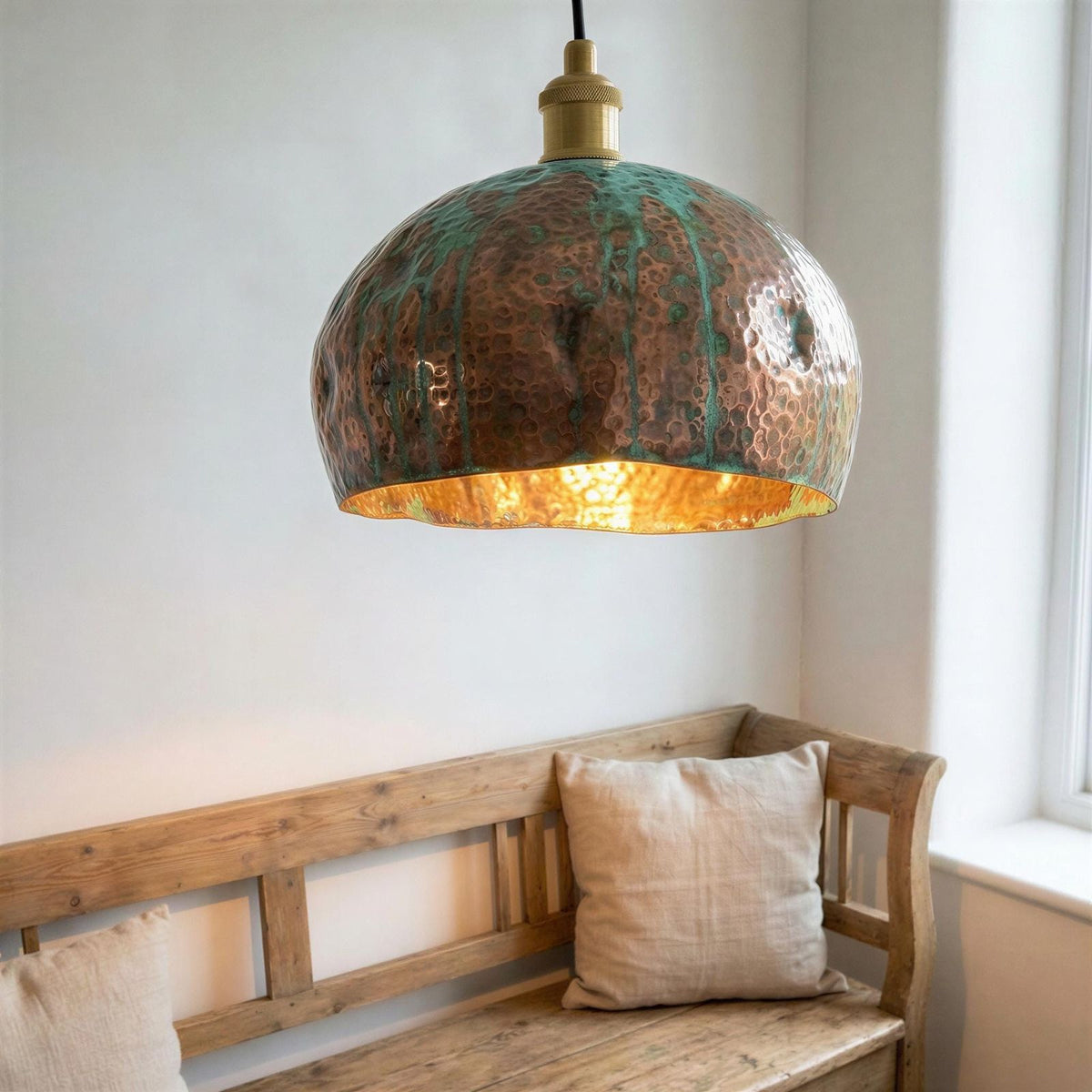 Copper pendant light hanging above a wooden bench with a pillow in a room.