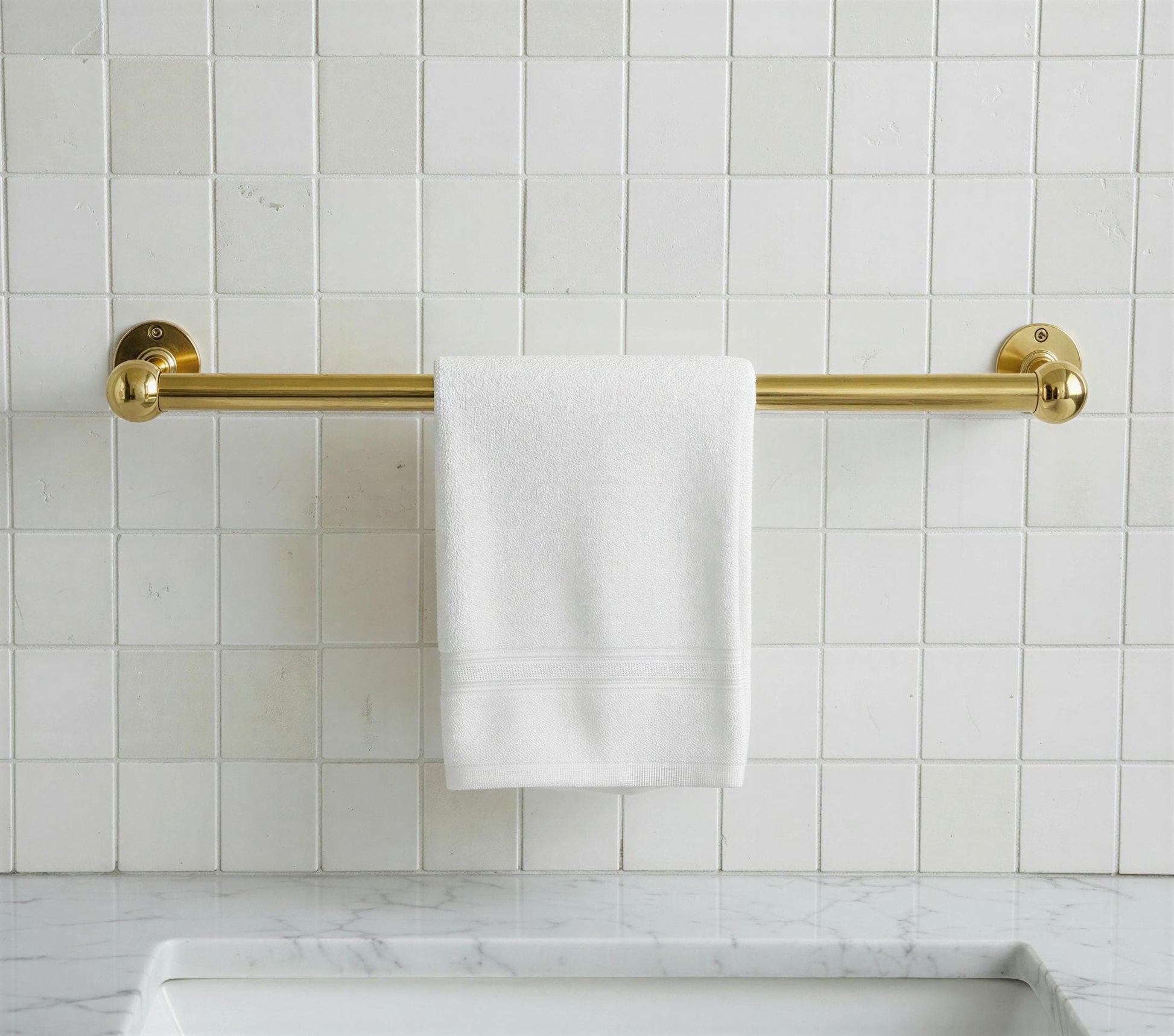 Gold towel rack with a white towel on a tiled bathroom wall.