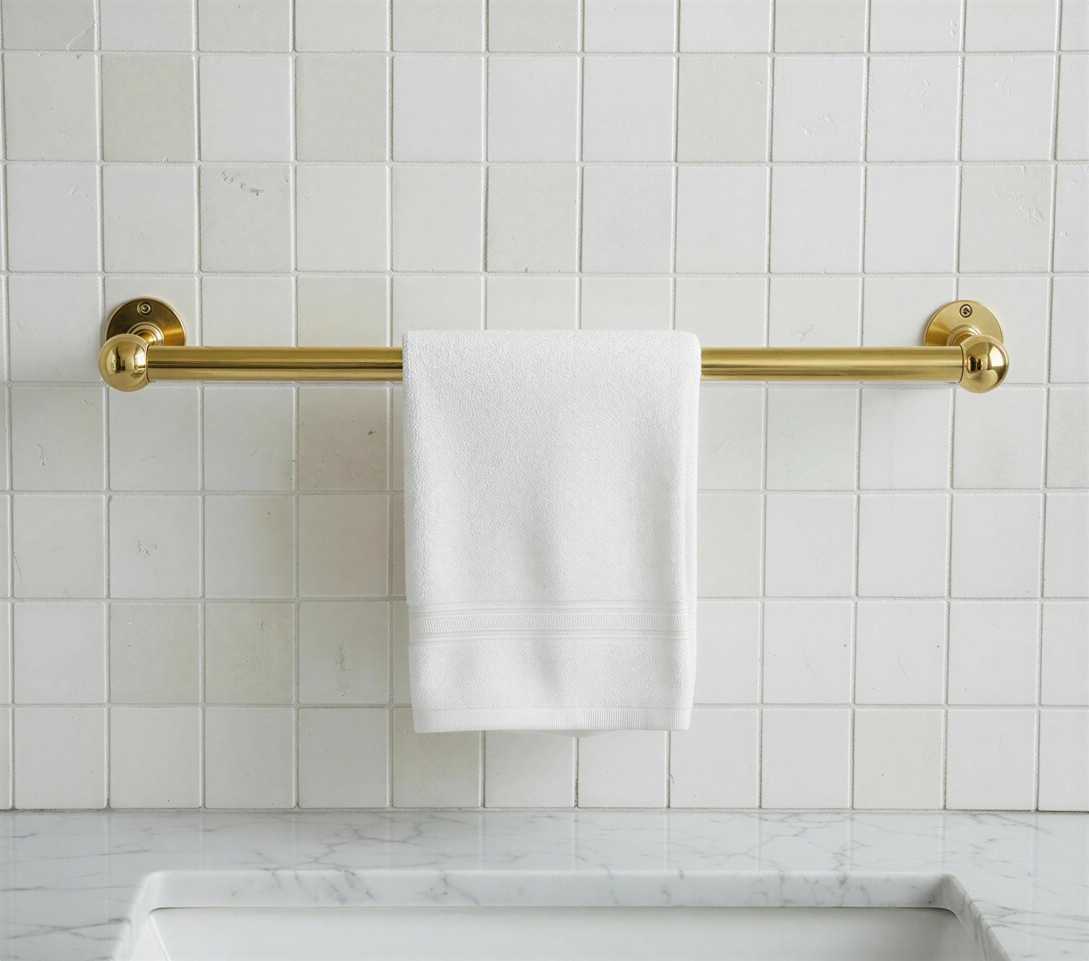 Gold towel rack with a white towel on a tiled bathroom wall.