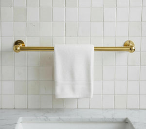 Gold towel rack with a white towel on a tiled bathroom wall.