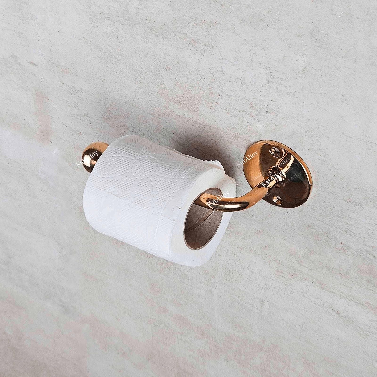 Rose gold toilet paper holder with a roll of toilet paper on a marble wall.