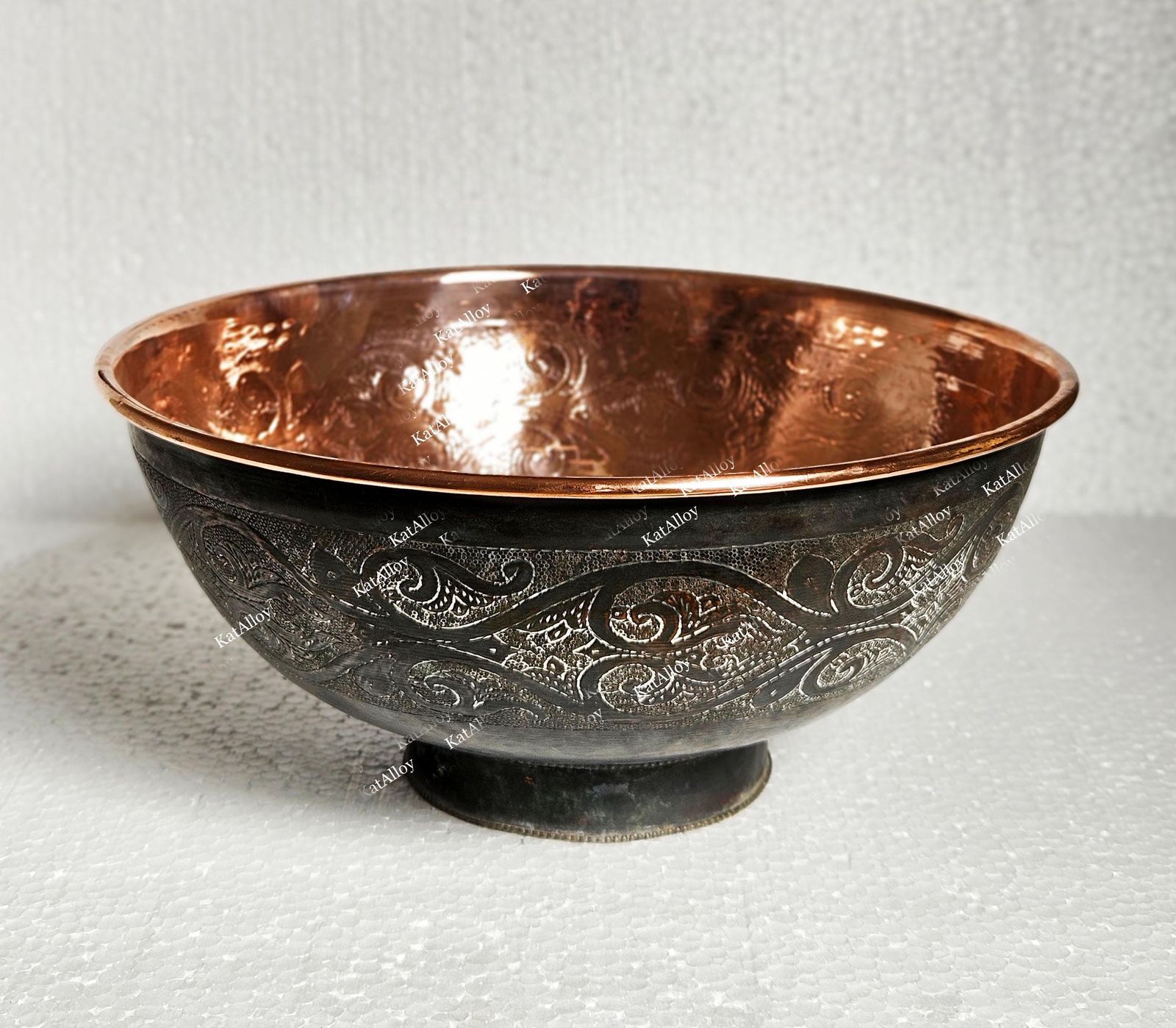 Copper bowl with engraved design on a textured white background