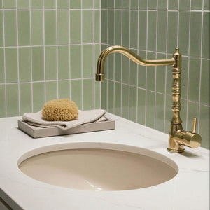 Bathroom sink with gold faucet and green tiled wall
