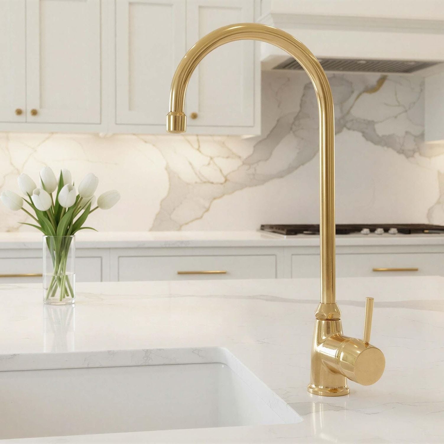 Gold kitchen faucet in a modern kitchen setting with marble backsplash and white cabinets.